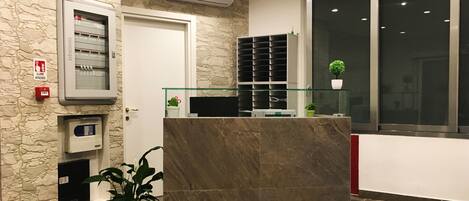 Un área de recepción con pared de piedra, mostrador de recepción, vitrina de vidrio y una planta en maceta.