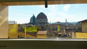 A view from inside a building, looking out at a cityscape with historical architecture, including a prominent dome and a tower.