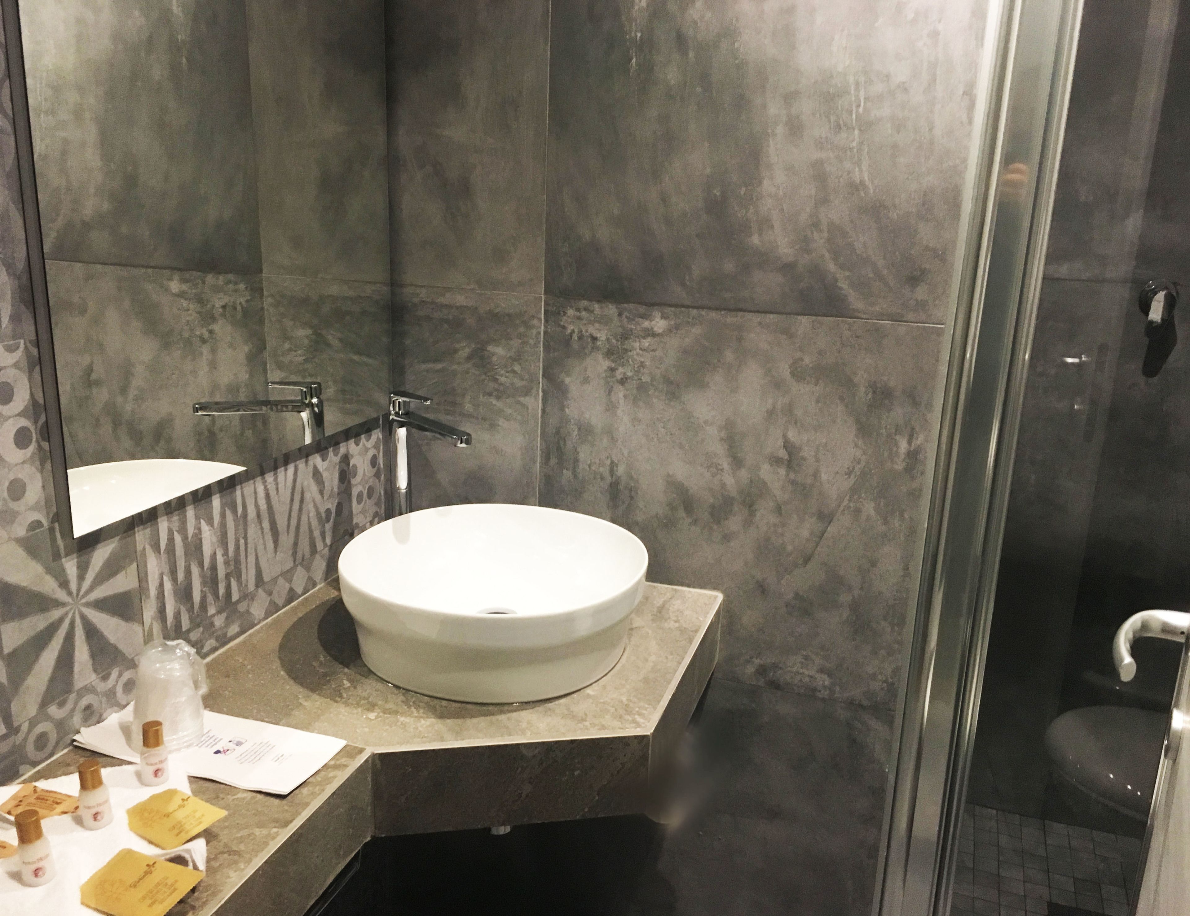 A modern bathroom with a round white sink, a mirror, and a shower area.