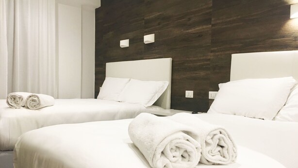 A hotel room with two beds, each with white linens and pillows, and a dark wood panel wall.