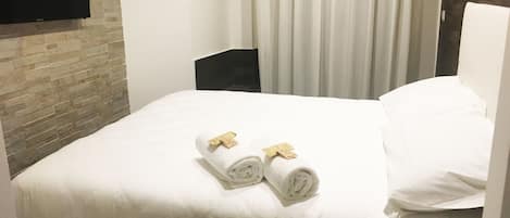 A hotel room with a large bed, a flat-screen TV mounted on the wall, and a remote control on the nightstand.