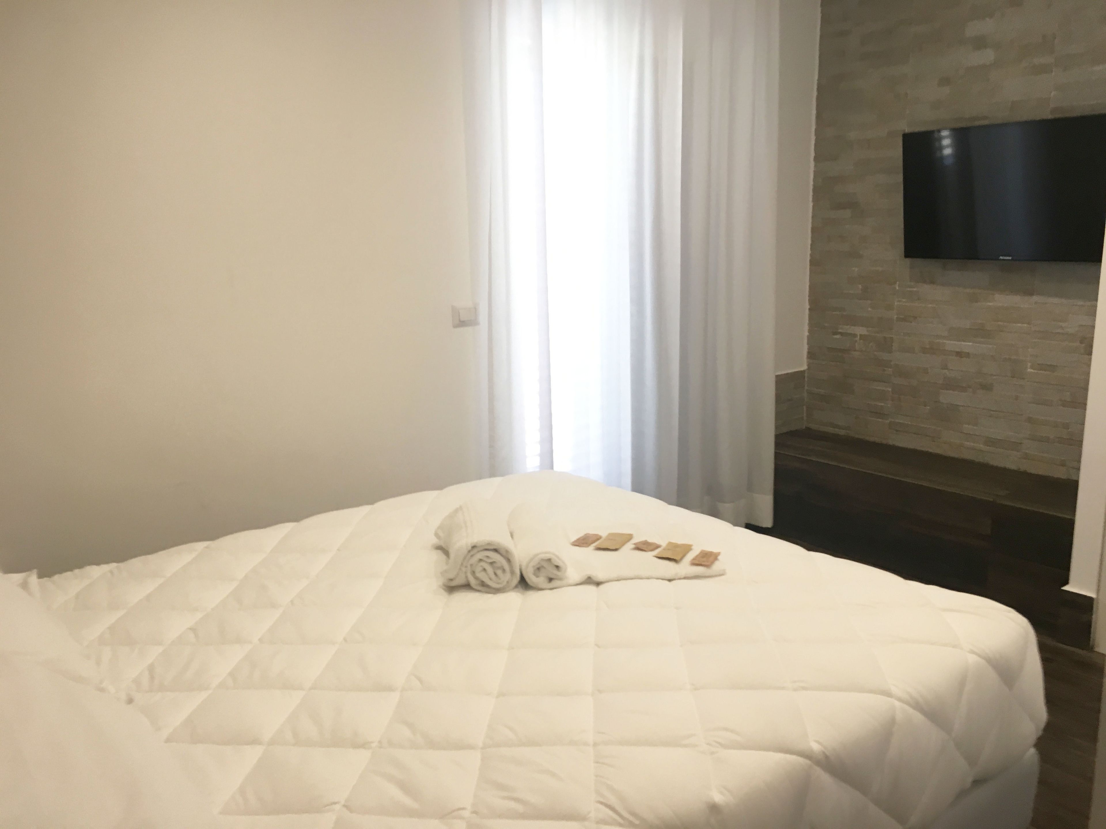 A neatly made bed with a quilted white duvet and rolled towels on it.