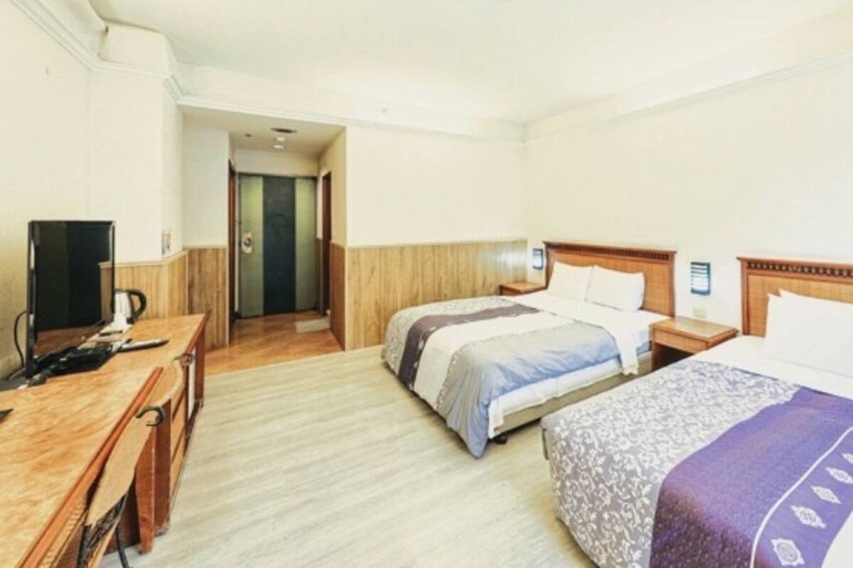 Una habitación de hotel con dos camas, un escritorio, una silla y un televisor.