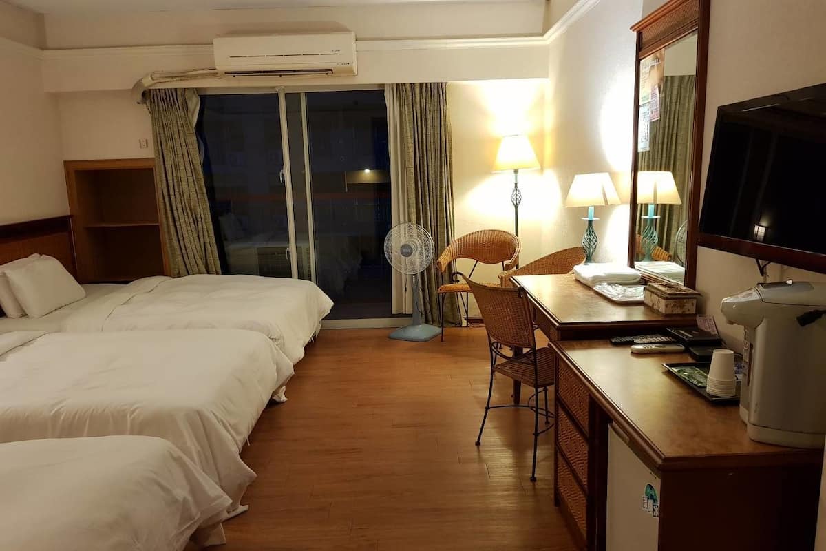 Habitación de hotel con dos camas, un escritorio con silla, televisor, ventilador y ventana con cortinas.