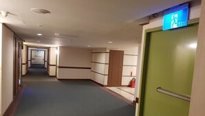 A hotel hallway with a green door, a fire extinguisher, and a blue exit sign. - Huya Hotel (Taimali)