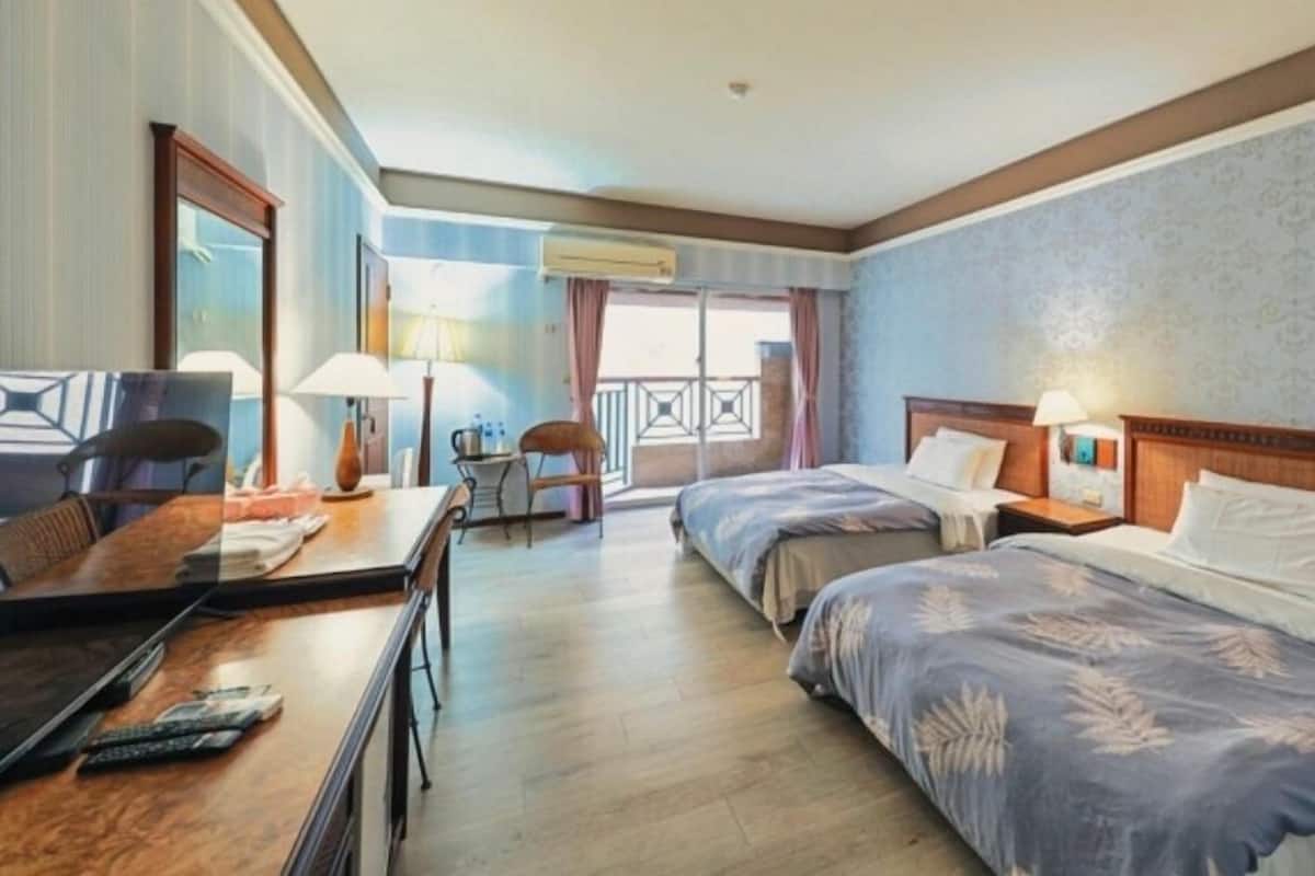 Habitación de hotel con dos camas, un escritorio, una silla y un balcón con vistas.