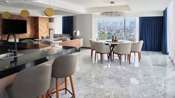 Une chambre d’hôtel moderne dotée d’un coin cuisine, d’un espace repas et d’une grande fenêtre donnant sur la ville.
