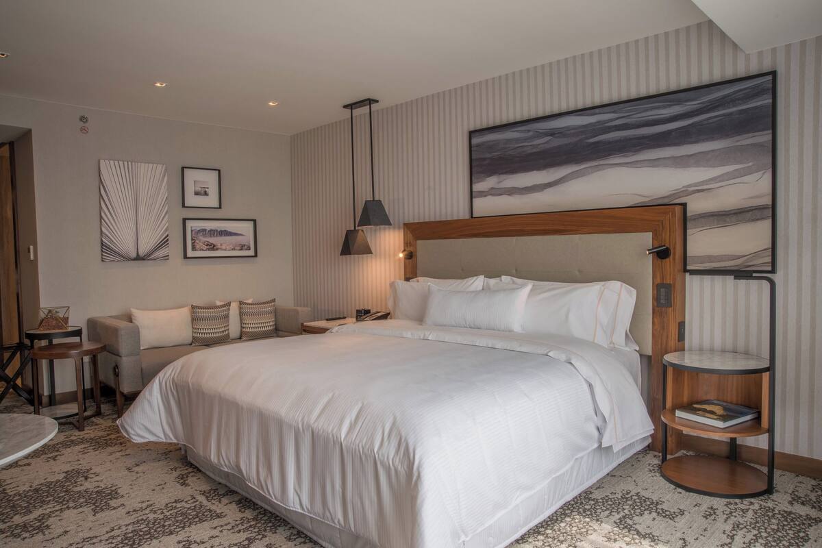 Une chambre d’hôtel moderne avec un grand lit, un canapé, une petite table et une étagère fixée au mur.