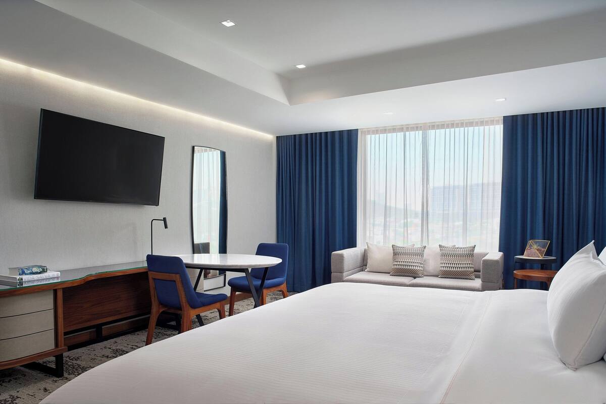 Une chambre d’hôtel avec un grand lit, un bureau avec une chaise, un téléviseur fixé au mur et une fenêtre avec des rideaux.