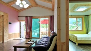 A cozy room with a wooden ceiling, a sofa, a bed, and a sliding glass door leading to an outdoor area with a red umbrella. - Hansoll Pension (Pyeongchang)