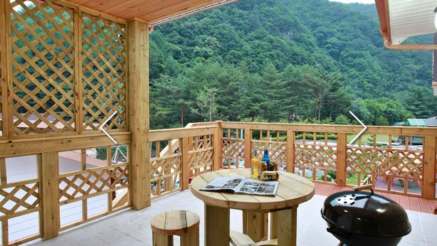 A wooden deck with a round table, a barbecue grill, and a bottle of alcohol. - Hansoll Pension (Pyeongchang)