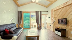 A cozy living room with a leather sofa, a wooden coffee table, and a television on a wooden wall. - Hansoll Pension (Pyeongchang)