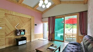 A room with wooden walls, a television, a sofa, a coffee table, and a sliding glass door leading to an outdoor area with a red umbrella. - Hansoll Pension (Pyeongchang)
