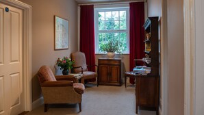 A cozy living room with a fireplace, a comfortable armchair, a small table with a vase of flowers, and a bookshelf. - The Saracen's Head (Norwich)