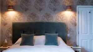 A neatly made bed with a large headboard, two pillows, and a bedside table with a lamp and a tissue box. - The Saracen's Head (Norwich)