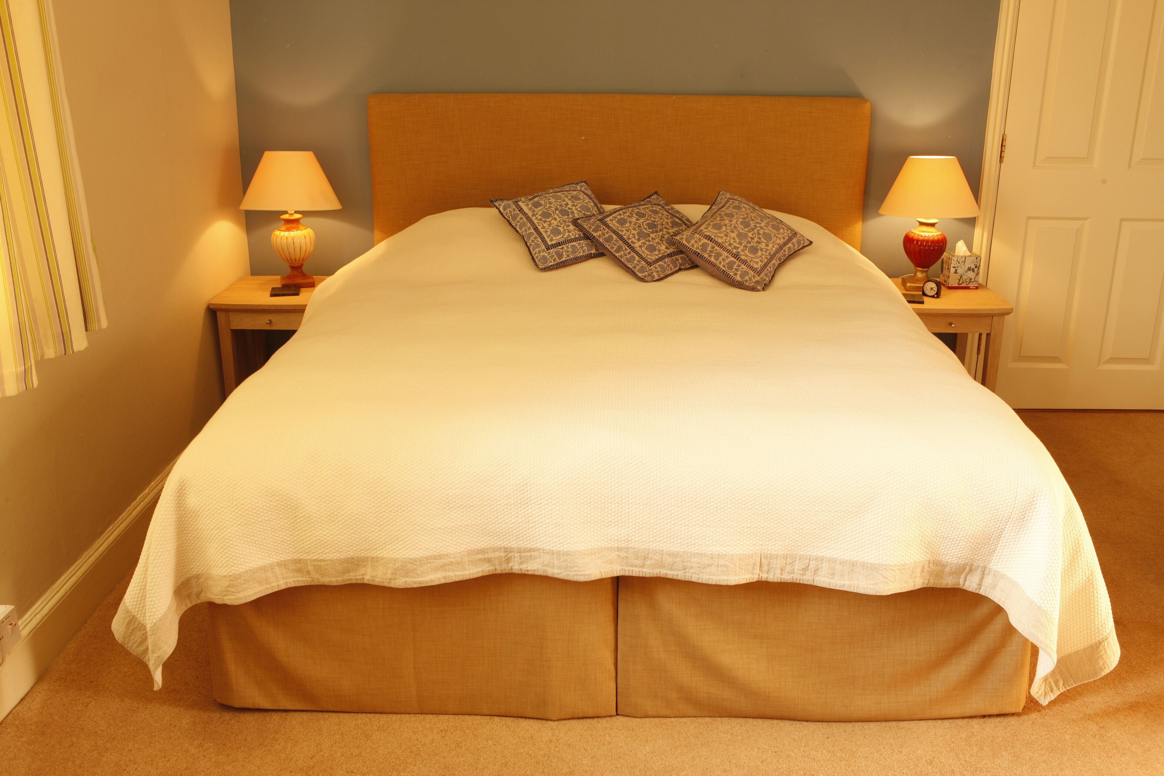 A neatly made bed with a white bedspread, two patterned pillows, and two bedside lamps on wooden nightstands.