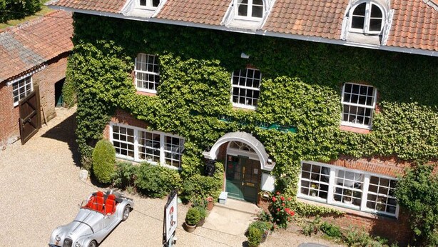 A two-story house with ivy-covered walls, a gravel driveway, and a red car parked in the front. - The Saracen's Head (Norwich)