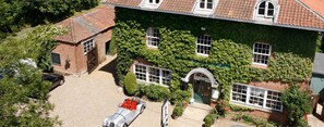 Ein zweistöckiges Haus mit Efeu bewachsene Wände, einer Schotterauffahrt und einem roten Auto vor der Fassade.