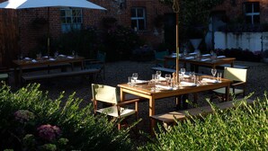 An outdoor dining area with wooden tables and chairs, white umbrellas, and a brick building in the background. - The Saracen's Head (Norwich)