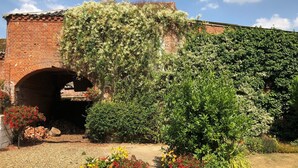 A brick building with an arched entrance, surrounded by lush greenery and potted plants. - The Saracen's Head (Norwich)