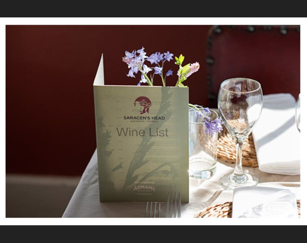 Eine Weinkarte mit der Aufschrift 'SARACEN'S HEAD' auf einem Tisch, zusammen mit einem Glas und einem Korb.