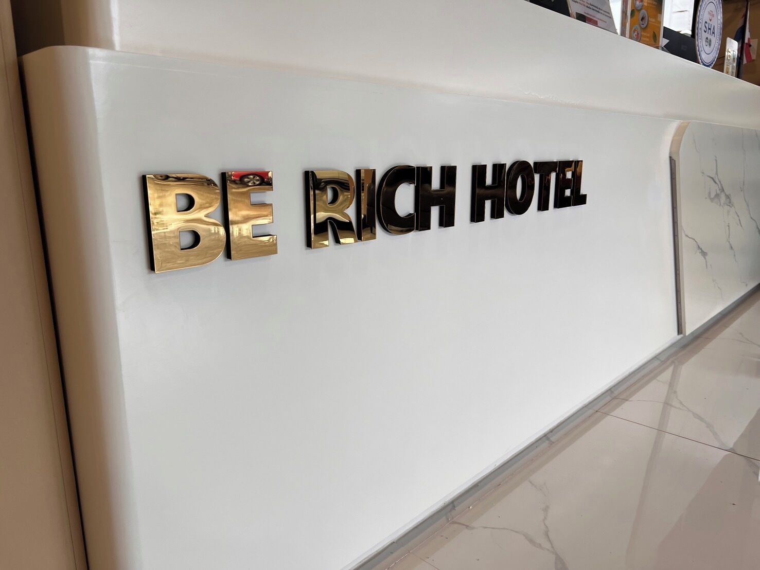Uma mesa de recepção com as palavras "BE RICH HOTEL" em letras metálicas.