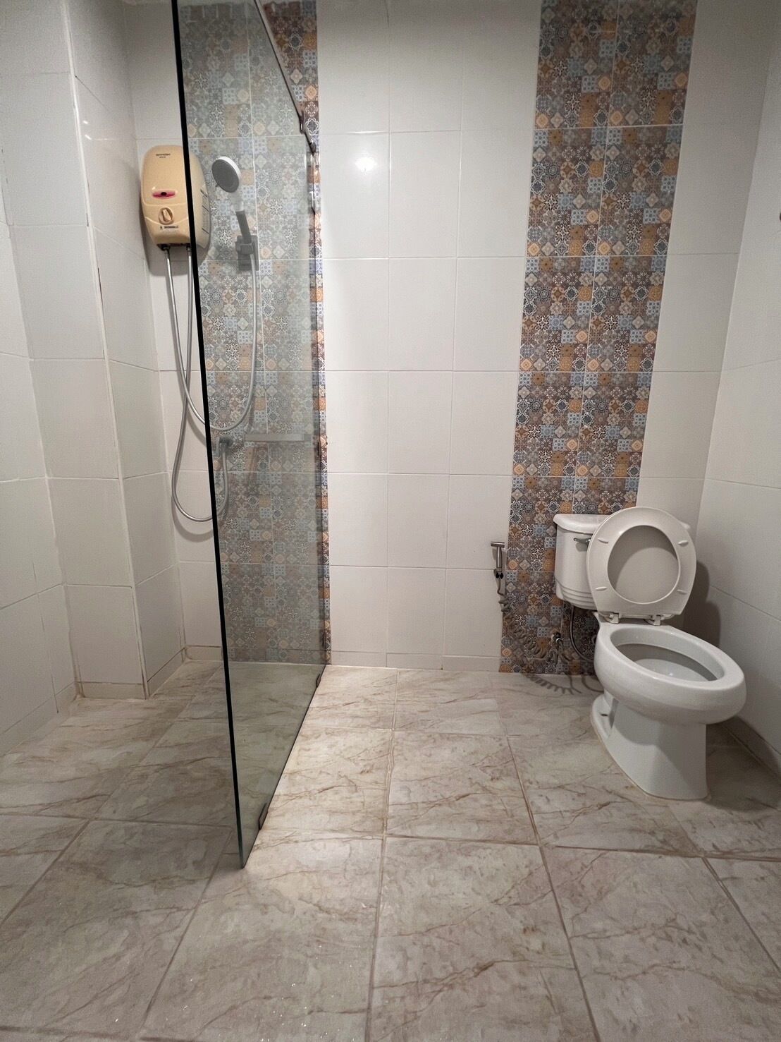 A bathroom with a glass shower enclosure, a toilet, and patterned tiles on the walls.