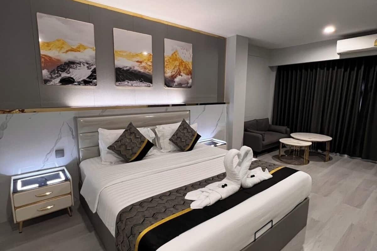 A modern hotel room with a large bed, a bedside table, a sofa, and a small round table.
