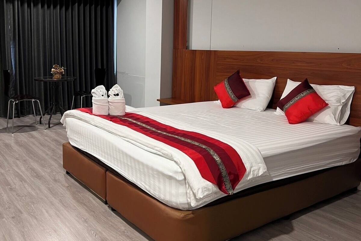 A modern hotel room with a large bed, wooden headboard, and a small table with towels.