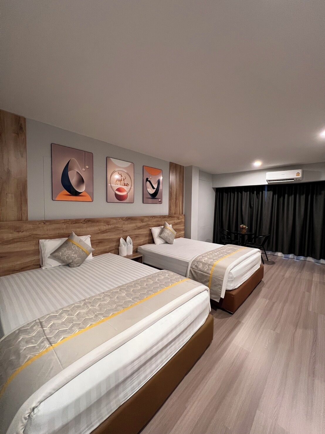 A hotel room with two beds, a wooden headboard, and three abstract wall art pieces.