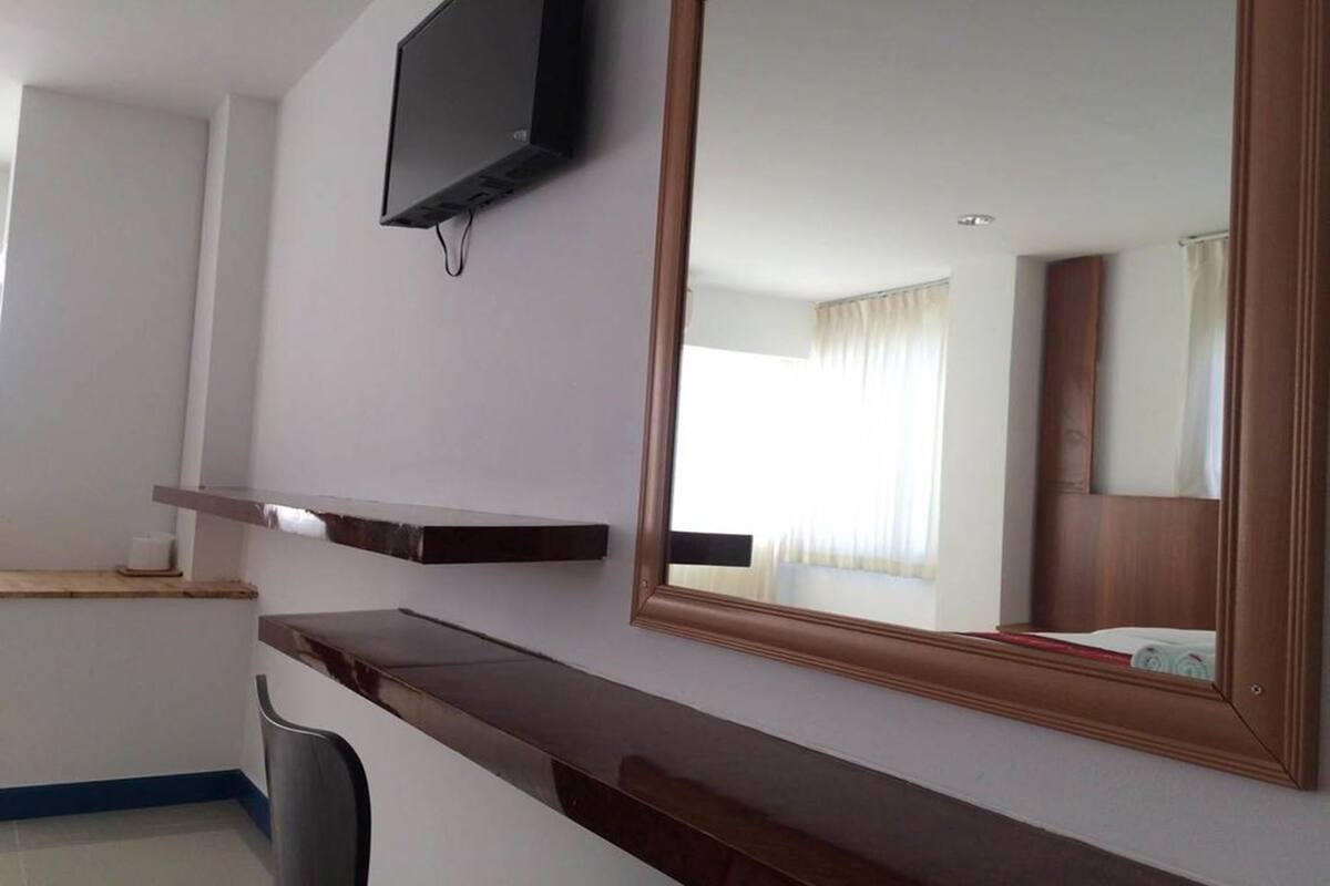 A hotel room with a large mirror, a flat-screen TV mounted on the wall, and a wooden shelf.