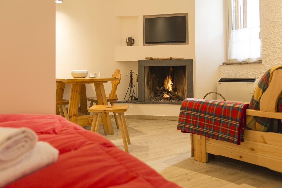 Um quarto acolhedor com lareira, uma cama, uma mesa de madeira com cadeiras e uma televisão na parede.