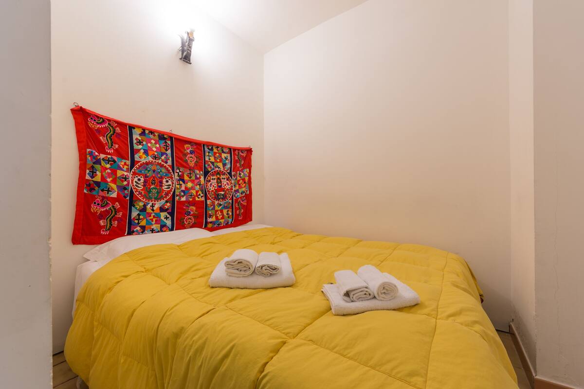 Cama com colcha amarela e duas toalhas enroladas.