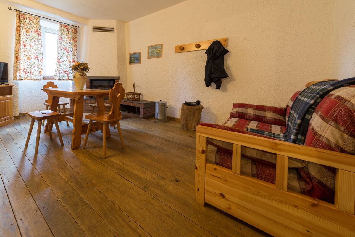 Uma sala de estar aconchegante com um sofá de madeira, uma mesa de jantar com cadeiras, uma televisão e uma lareira.