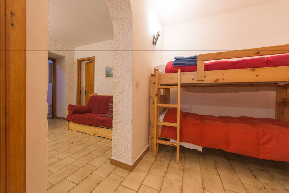 Quarto com beliche, sofá e piso de madeira.