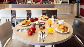 A breakfast setting with a table set for two, including croissants, fruit, cereal, and juice.