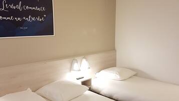 Une chambre d’hôtel avec deux lits, une table de chevet avec une lampe et une citation affichée sur le mur.