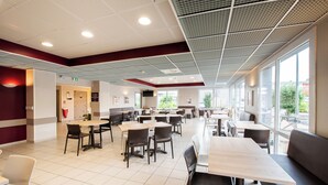 A spacious cafeteria with multiple tables and chairs, large windows, and a high ceiling with grid patterns. - ACE Hôtel Toulouse (Cornebarrieu)