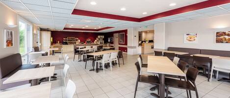 A modern dining area with multiple tables and booths, a kitchen in the background, and a red accent wall.