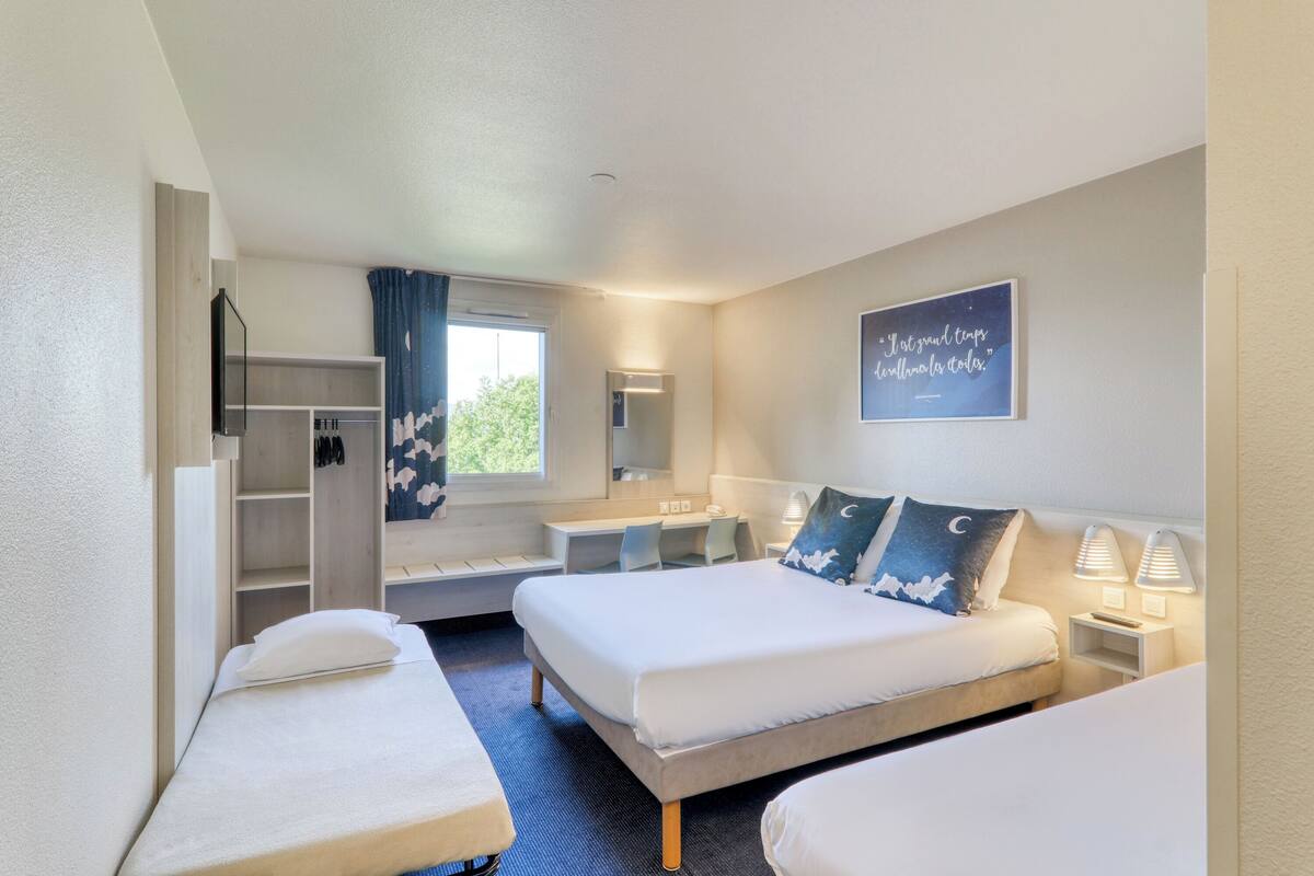 A hotel room with two beds, a desk, a wardrobe, and a window with curtains.