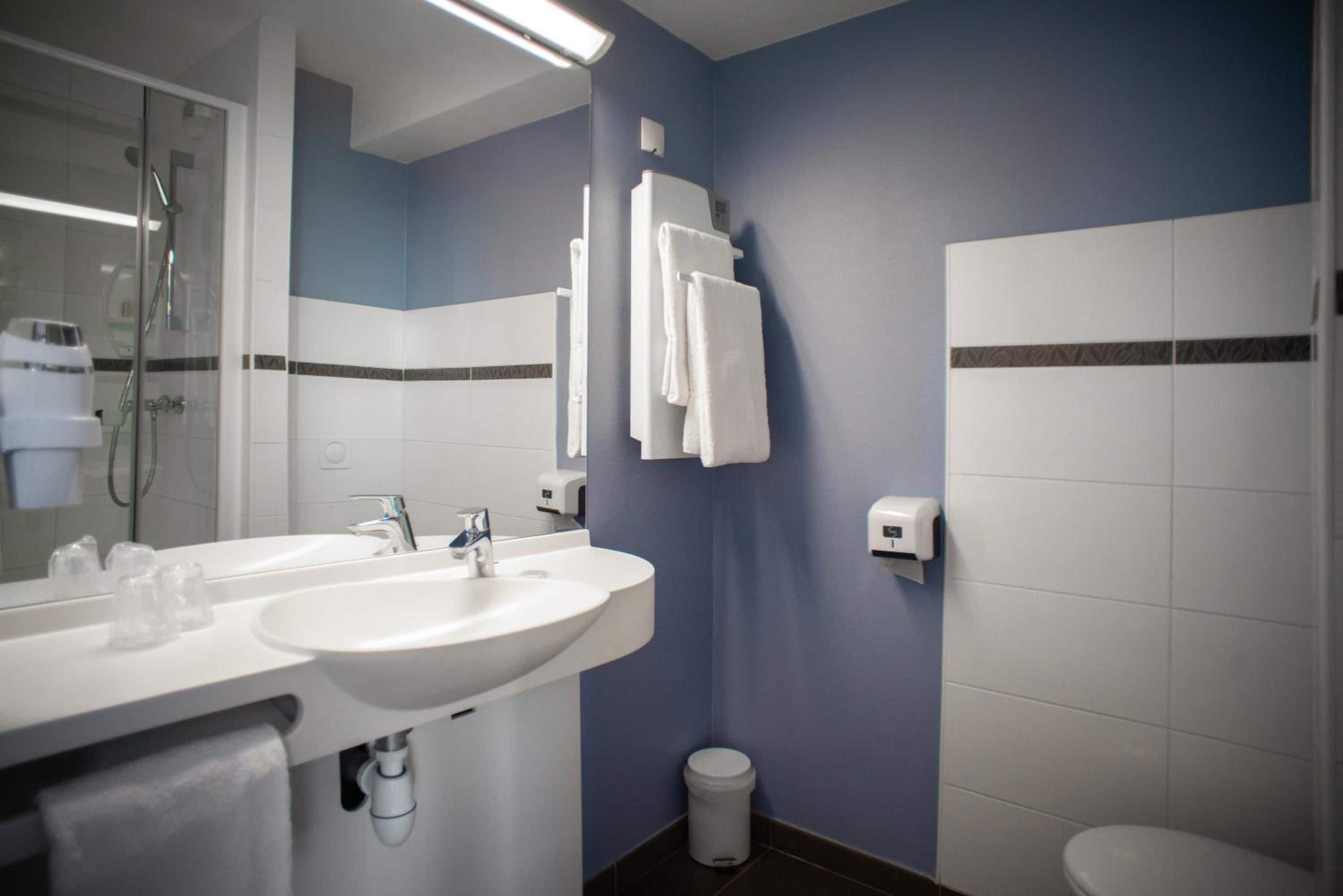 Een badkamer met een dubbele wastafel, een spiegel, een handdoekhouder, een handdroger en een toilet.