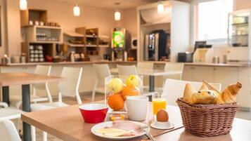 A breakfast setup with a plate of food, a basket of bread, a glass of orange juice, and a bowl of fruit.