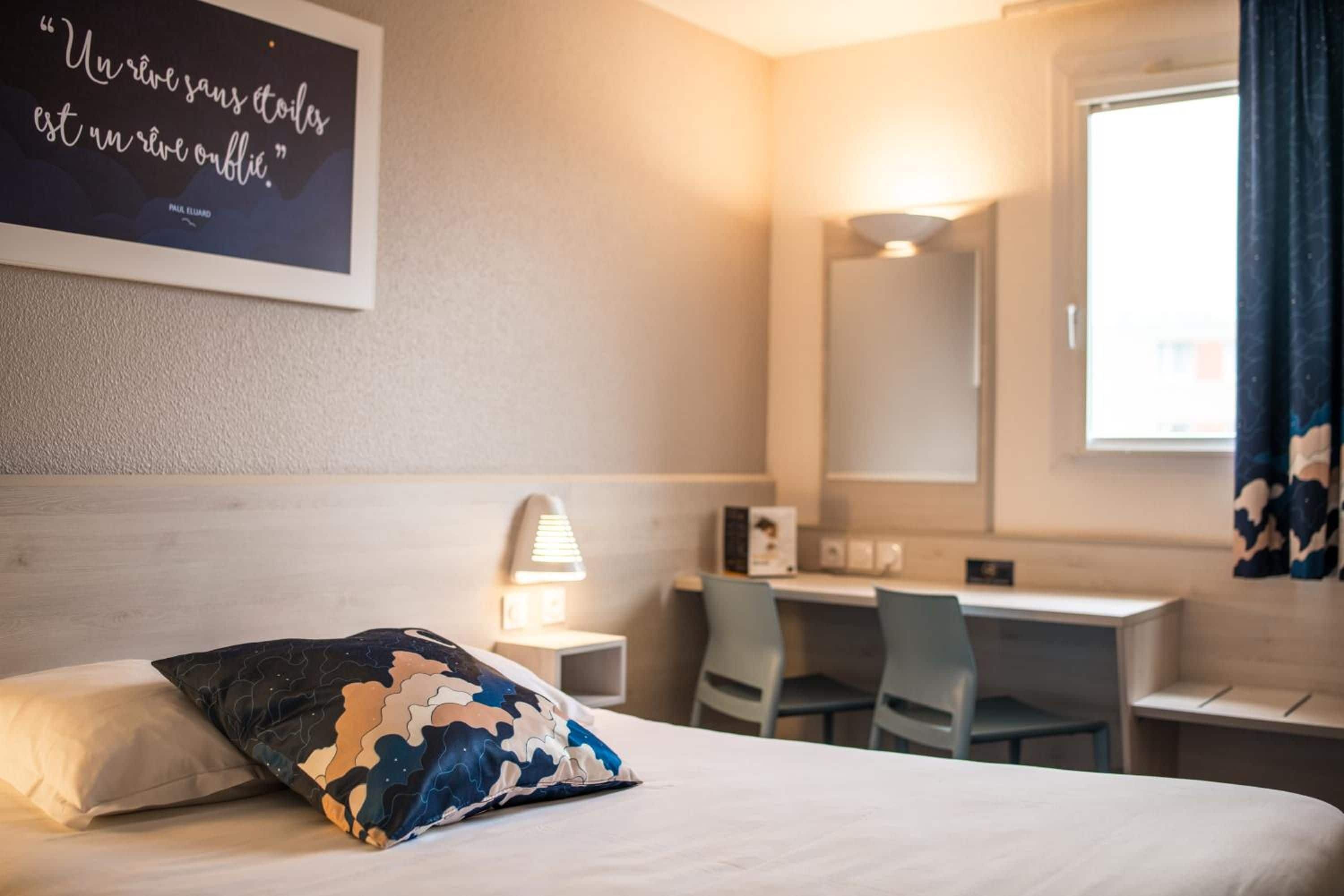 Habitación de hotel con cama, escritorio, silla, lámpara y una pared con una cita.