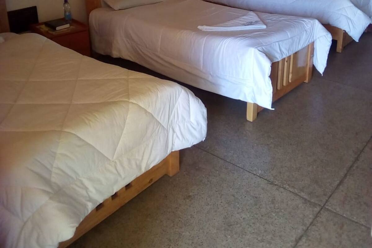 A room with three wooden beds, a wooden nightstand with a water bottle, and a wooden door.