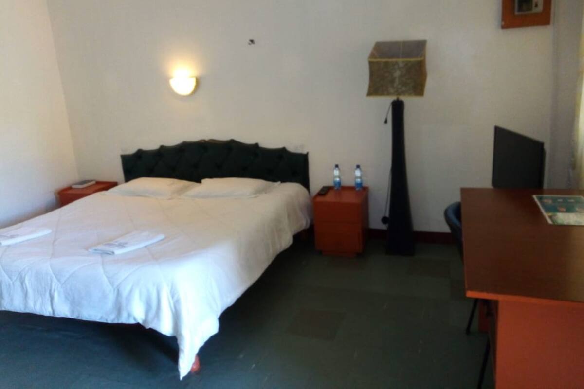 A hotel room with a bed, bedside tables, a desk, a lamp, and a wall-mounted light.