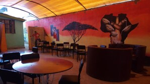 A dining area with a round table and chairs, a mural on the wall, and a large planter. - Family Comfort Hotel (Nanyuki)