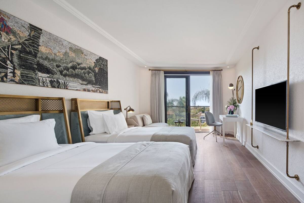 Habitación de hotel con dos camas, un escritorio, un televisor y un balcón con vistas.