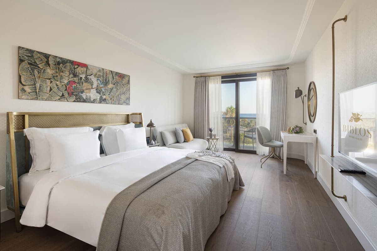 Una habitación de hotel con una cama grande, un escritorio, una silla y un balcón con cortinas.