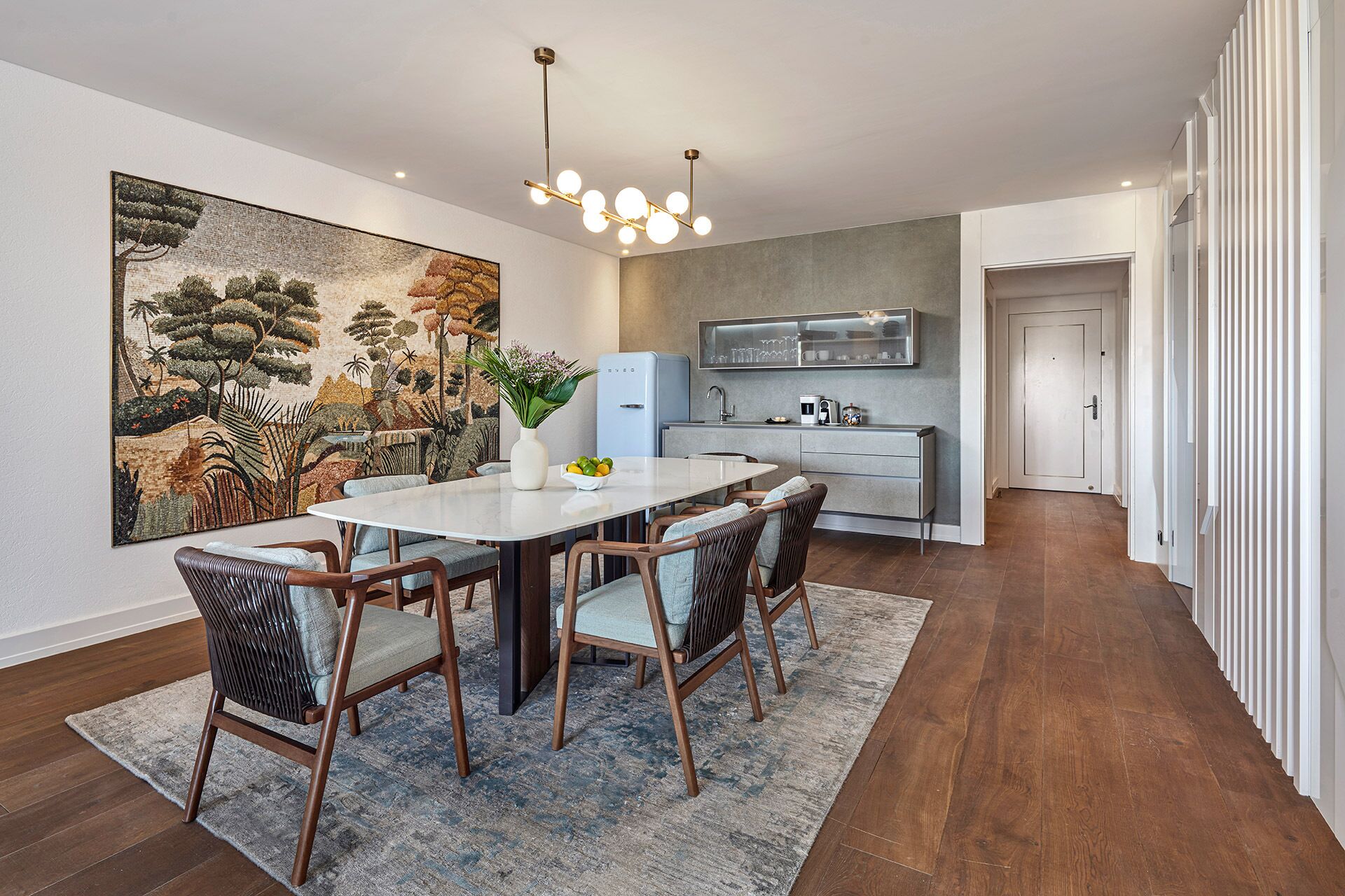 A modern kitchen with a built-in oven, a dining area with a round table and four chairs, and a large abstract painting on the wall.