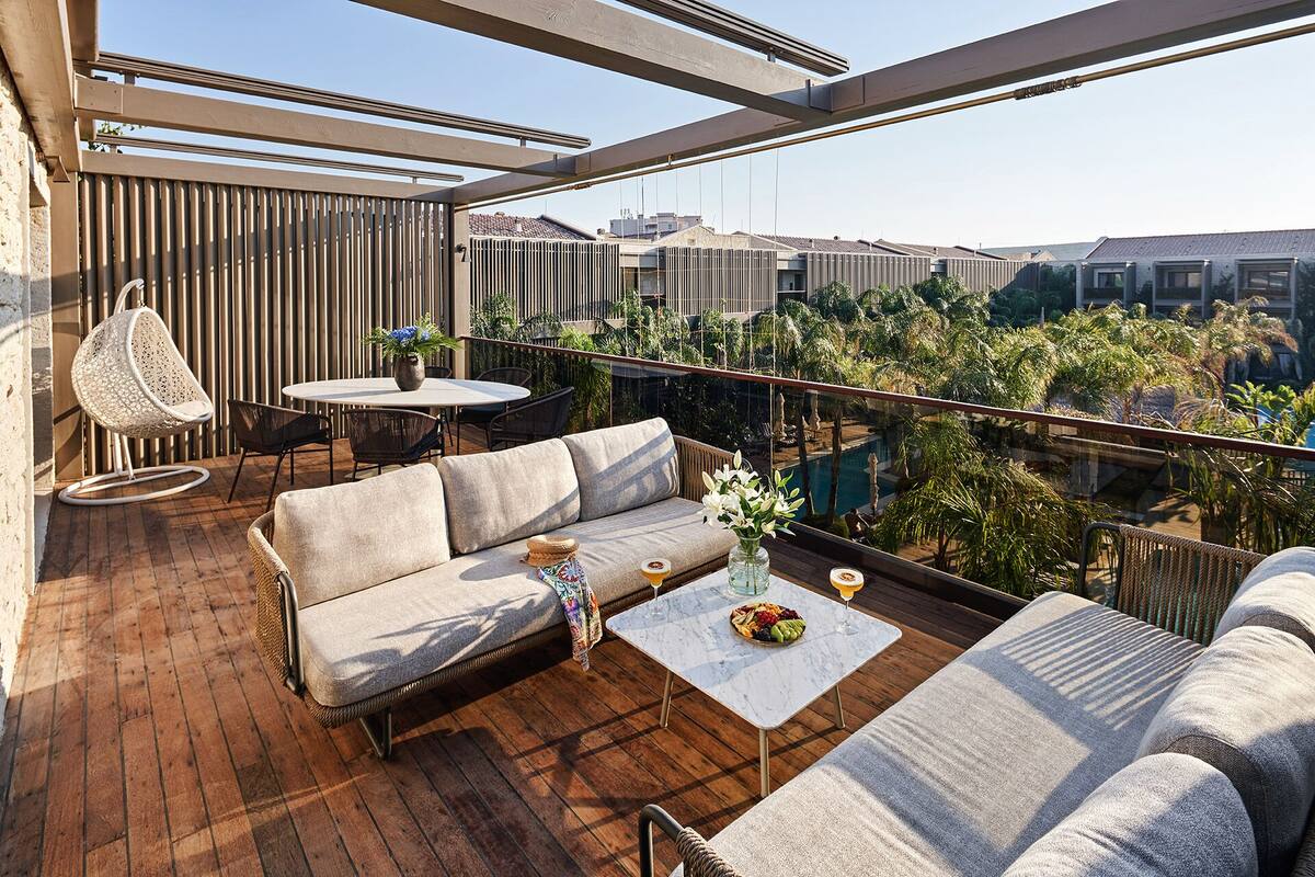Un balcón moderno con piso de madera, un sofá, una mesa de comedor y una silla colgante.